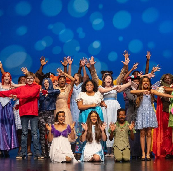 Student performers dressed as various fairytale characters pose on stage